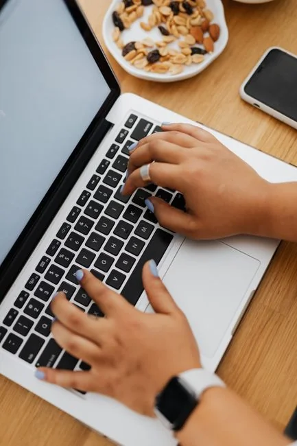 Hands using smartphone beside laptop with stock charts, showcasing digital trading.